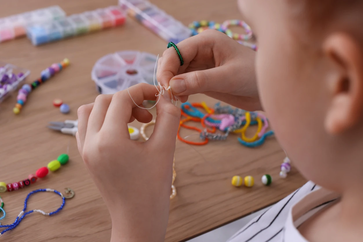 Little girl making beaded jewelry at table, closeup
