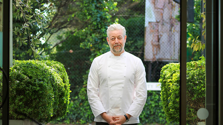 Chef Adam Byatt in chef whites standing in front of green bushes