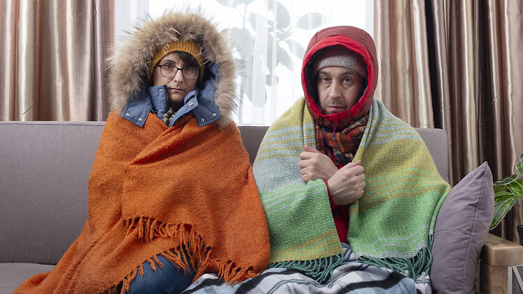 Middle age couple in warm clothes getting cold on the sofa in their living room