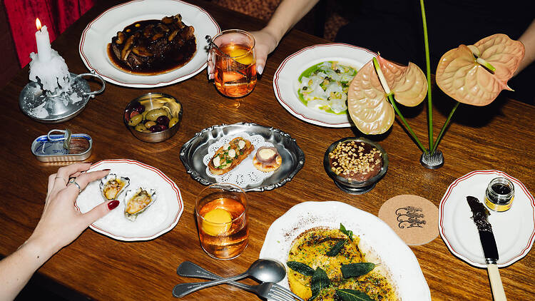 A table of dishes and Old Fashioned cocktails in a low-lit restaurant