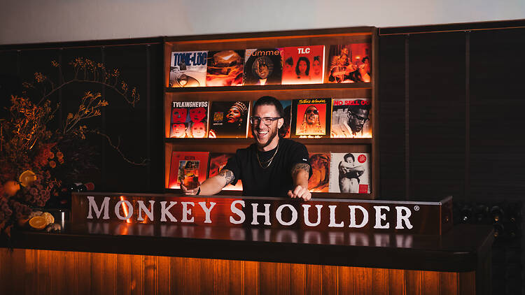 A man posing behind a sign that reads Monkey Shoulder