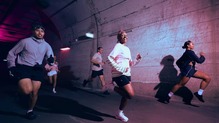 People running through a neon-lit tunnel