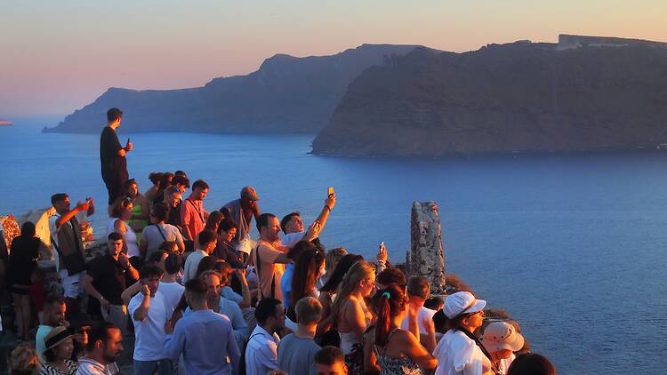 A crowd of tourists watch the spectacular Oia sunset from the walls of the Venetian Castle; it is one of the main attractions of the Greek island