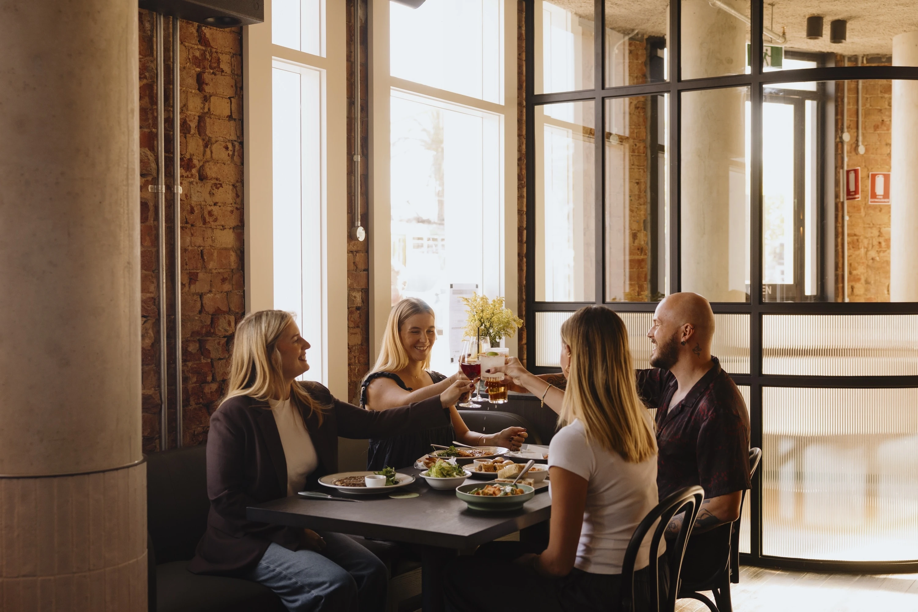 Group of pub guests clinking drinks over a table of food.