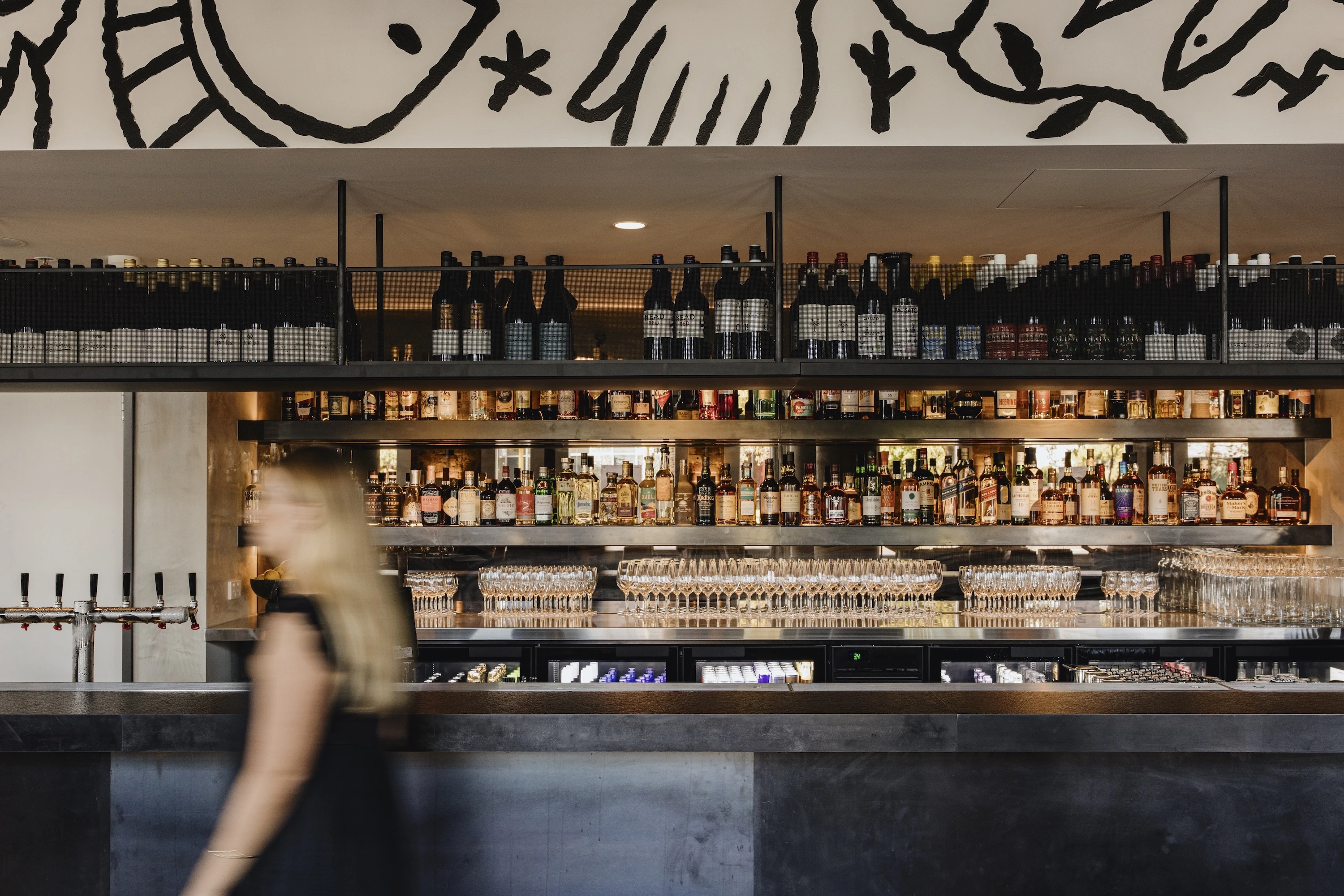 Waitress walking in front of a well-stocked bar.