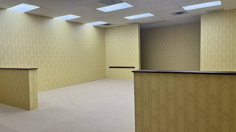 A24 Backrooms experience A room with yellow wallpaper and beige carpet.