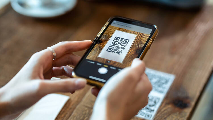 Woman using smart phone to scan the qr code in restaurant. Close up of young woman hands using the smart phone to scan the qr code to select food menu in the restaurant.