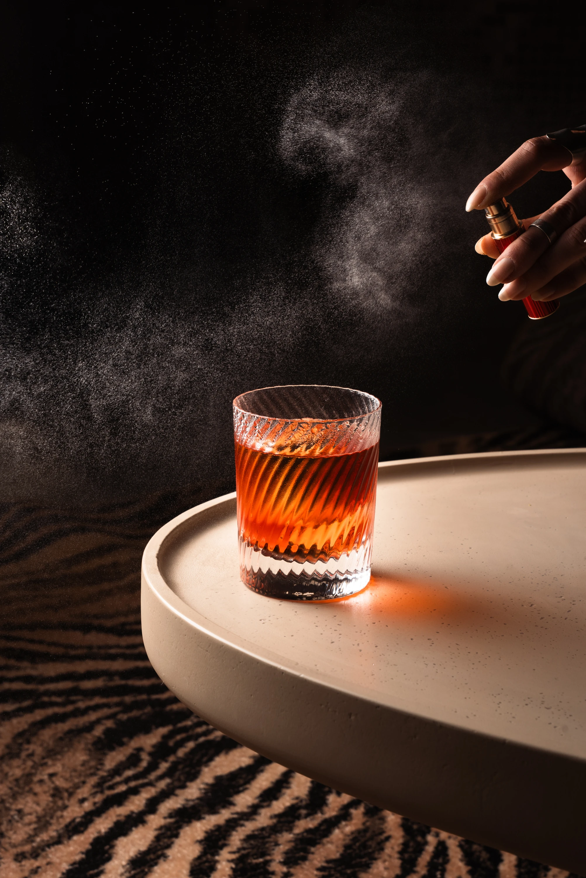 Classic negroni on table edge with hand spraying perfume onto drink