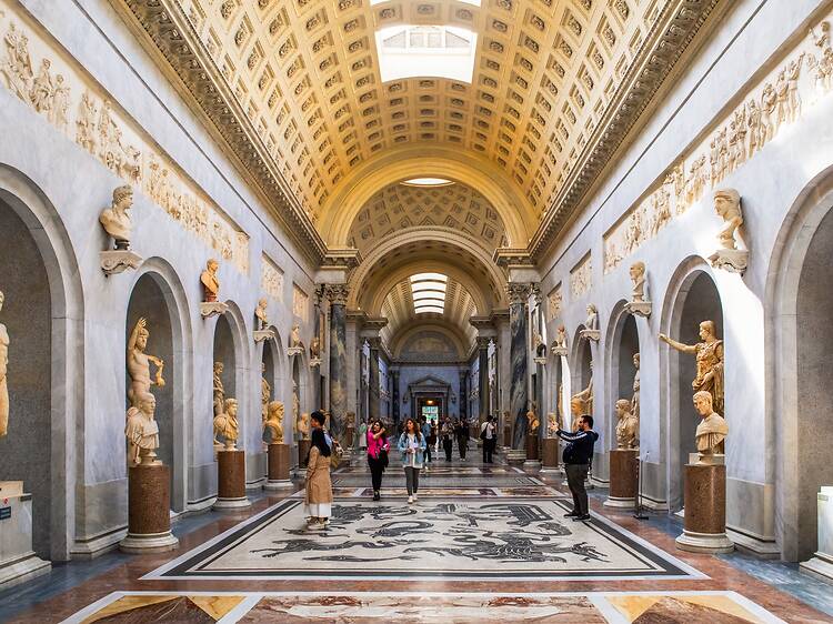 A corridor inside the Vatican Museums showcasing ancient Roman and Greek statues A corridor inside the Vatican Museums showcasing ancient Roman and Greek statues