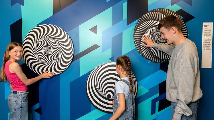 Three people try out the spinning discs at the Museum of Illusions 