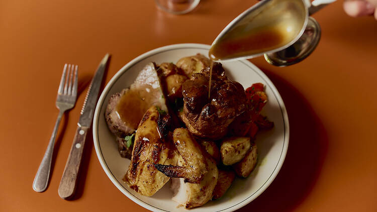 Gravy being poured over a plate of roast and veggies.