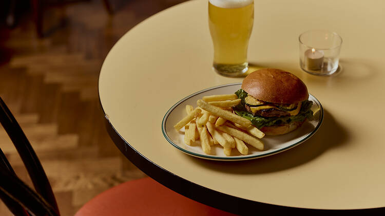 A cheeseburger and chips on a table next to a pint of beer.