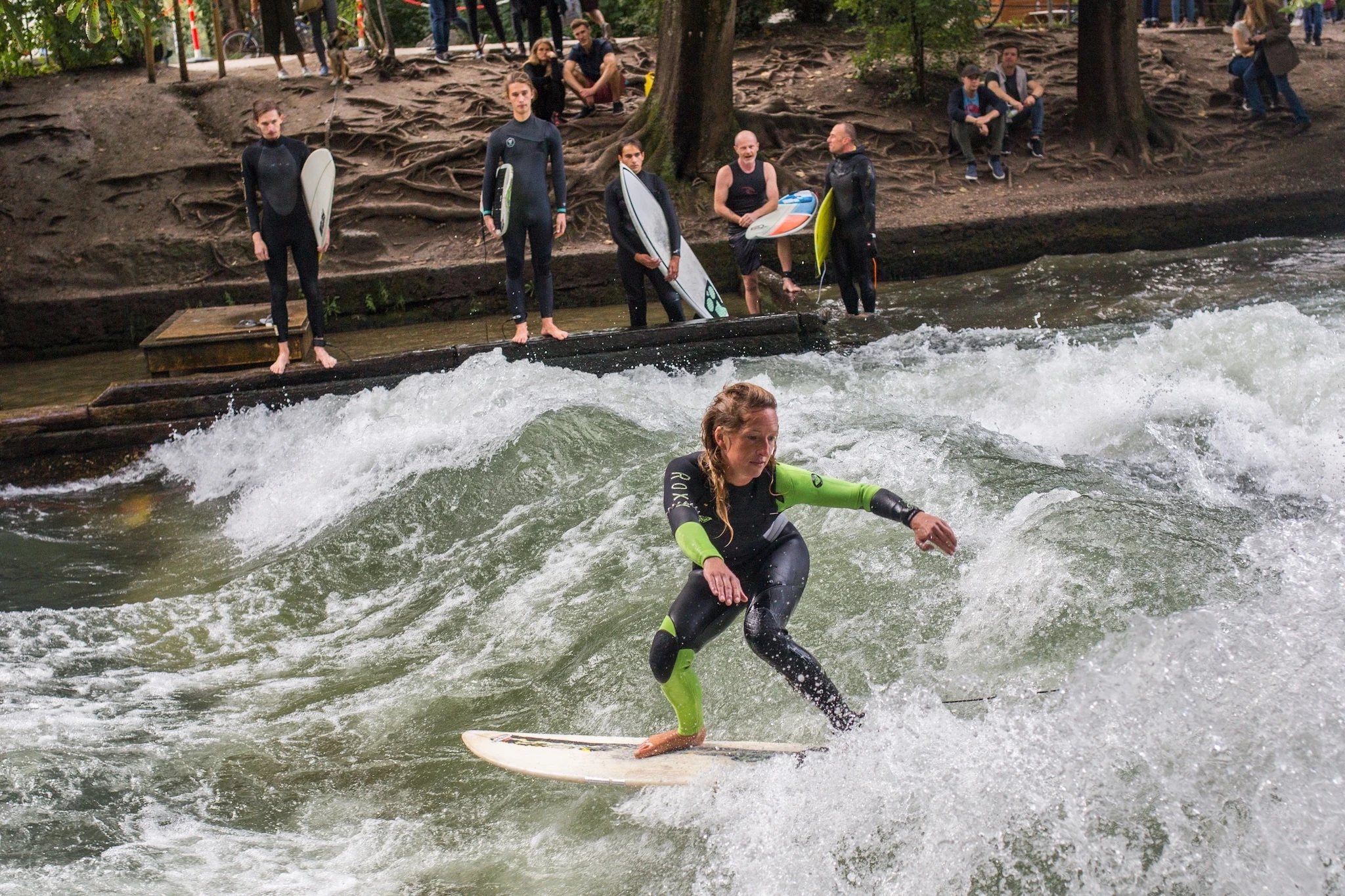 Surfers ride on Eisbachwelle - an artificial wave on the river Eisbach in the center of Munich