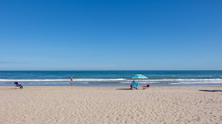 People enjoying summer vacation on the expansive sandy beach with clear blue sky People enjoying summer vacation on the expansive sandy beach with clear blue sky
