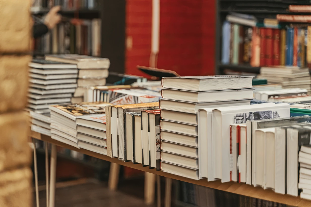 Stacks of hardcover books displayed on bookstore tables during busy literary season. Bookstore atmosphere evokes passion, curiosity and timeless love for books