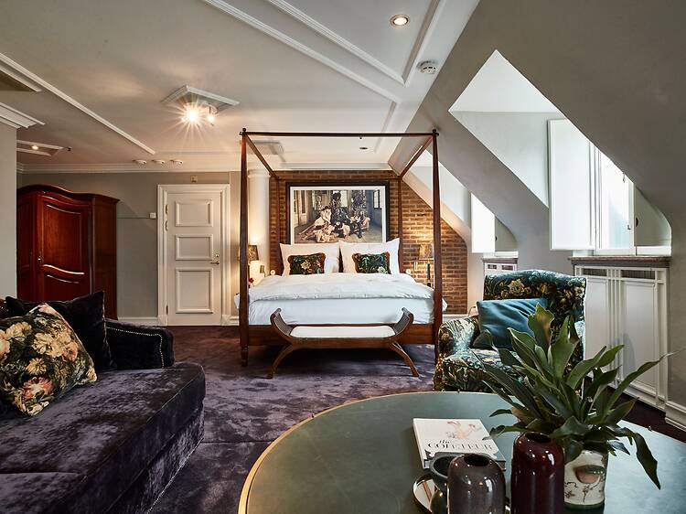 Ett elegant hotellrum med en säng med himmelssängram, sammetsmöbler och dekorativa detaljer skapar en varm och lyxig atmosfär. Ett elegant hotellrum med en säng med himmelssängram, sammetsmöbler och dekorativa detaljer skapar en varm och lyxig atmosfär.