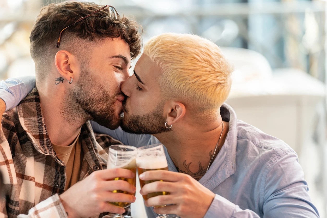 Fashionable gay couple on a date, spending time together, kissing, drinking beer. Real people lifestyle. Love. Handsome guys.