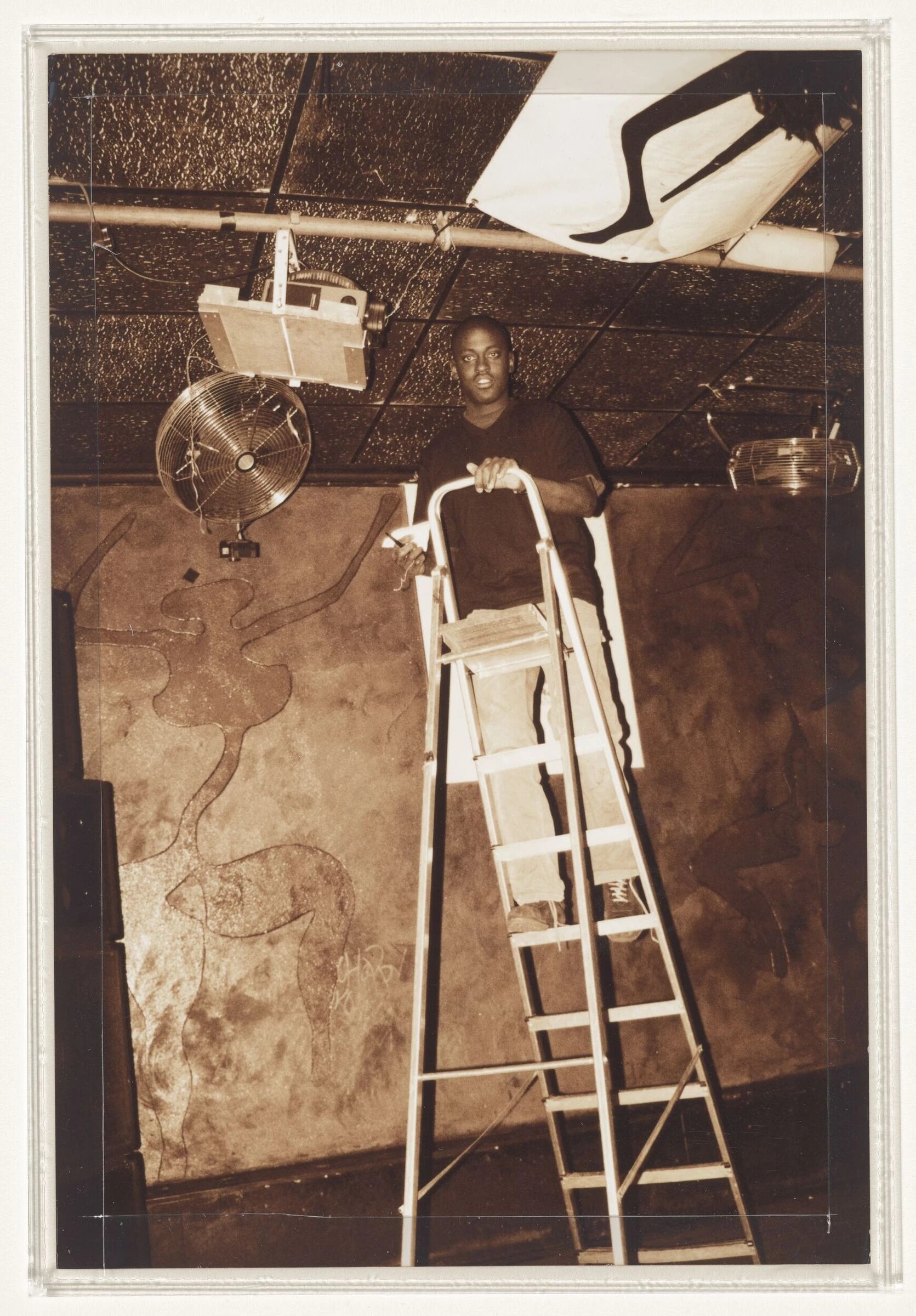 Sepia photograph of Ade Fakile on a ladder fixing projector in London club Plastic People