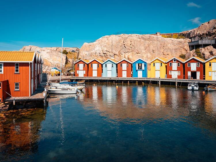Colorful wooden fishing huts line a calm harbor with small boats and rocky cliffs under a clear blue sky in Smögen, Sweden Colorful wooden fishing huts line a calm harbor with small boats and rocky cliffs under a clear blue sky in Smögen, Sweden