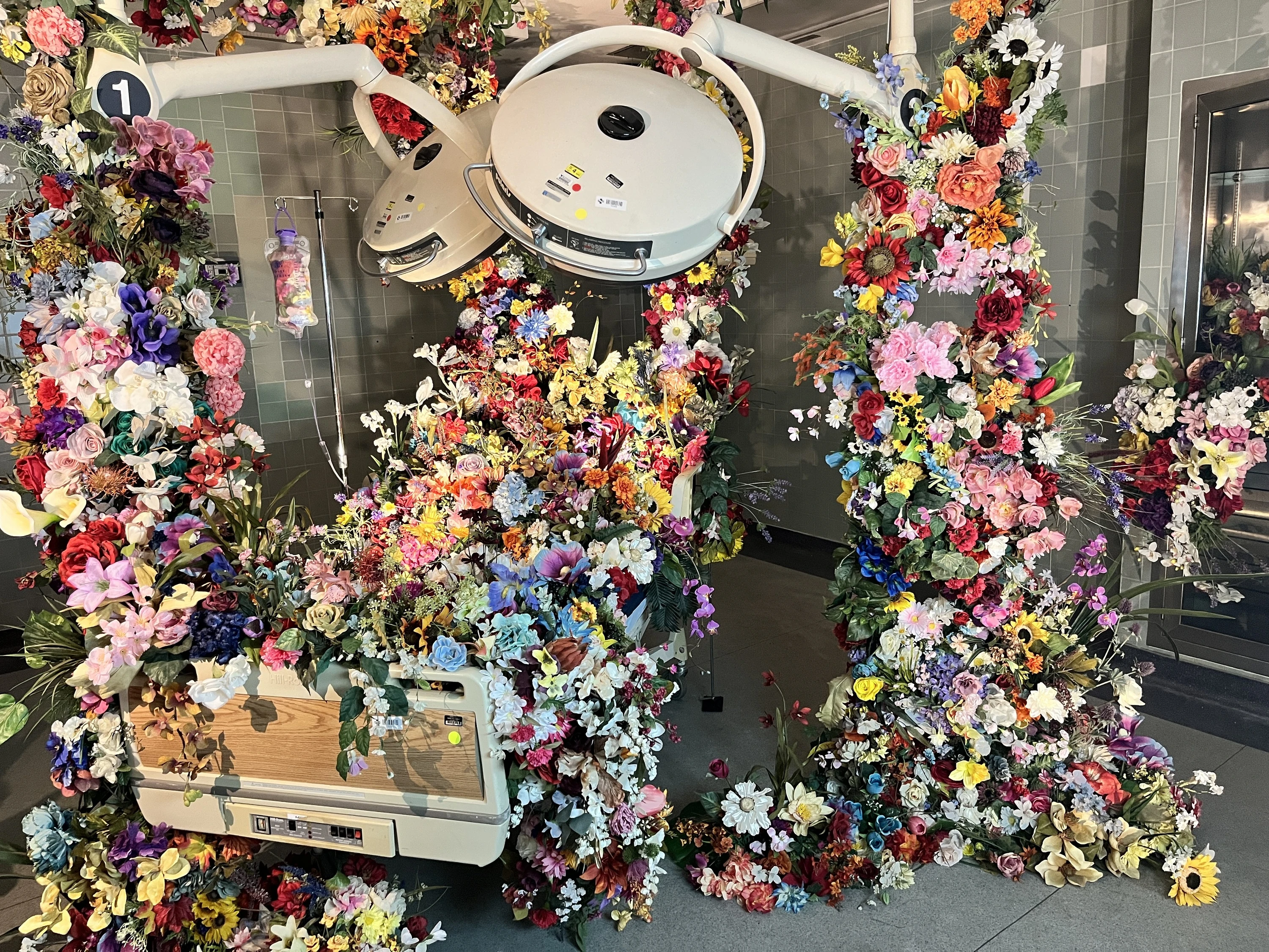 A hospital bed covered in faux flowers at Hospital of Emotions.