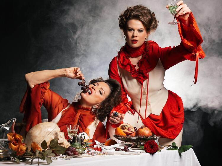 Kaksi punavalkoisiin pukeutunutta naista syö pröystäillen ruokaa teatteriesitykesssä Kaksi punavalkoisiin pukeutunutta naista syö pröystäillen ruokaa teatteriesitykesssä