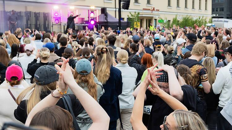 Ihmiset Lasipalatsin aukiolla kuuntelemassa keikkaa Ihmiset Lasipalatsin aukiolla kuuntelemassa keikkaa