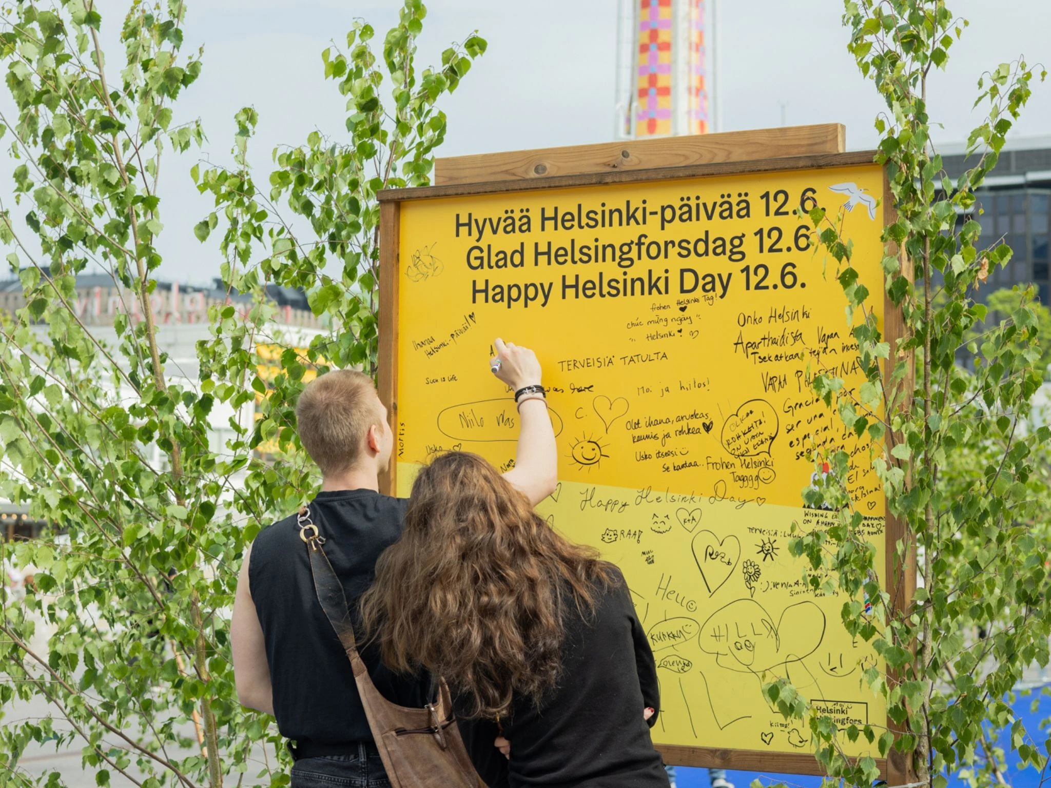 Mies ja nainen kirjoittavat syntym&auml;p&auml;iv&auml;tervehdyst&auml; keltaiseen tauluun Helsinki-p&auml;iv&auml;n&auml;