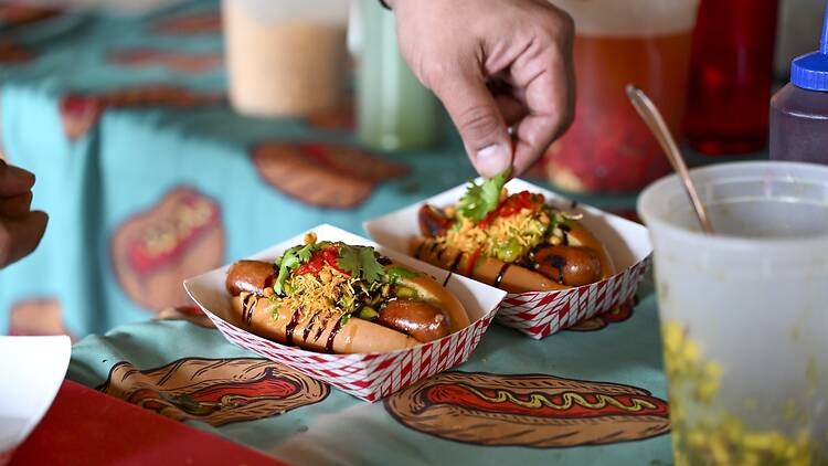 A person putting cilantro on a hot dog