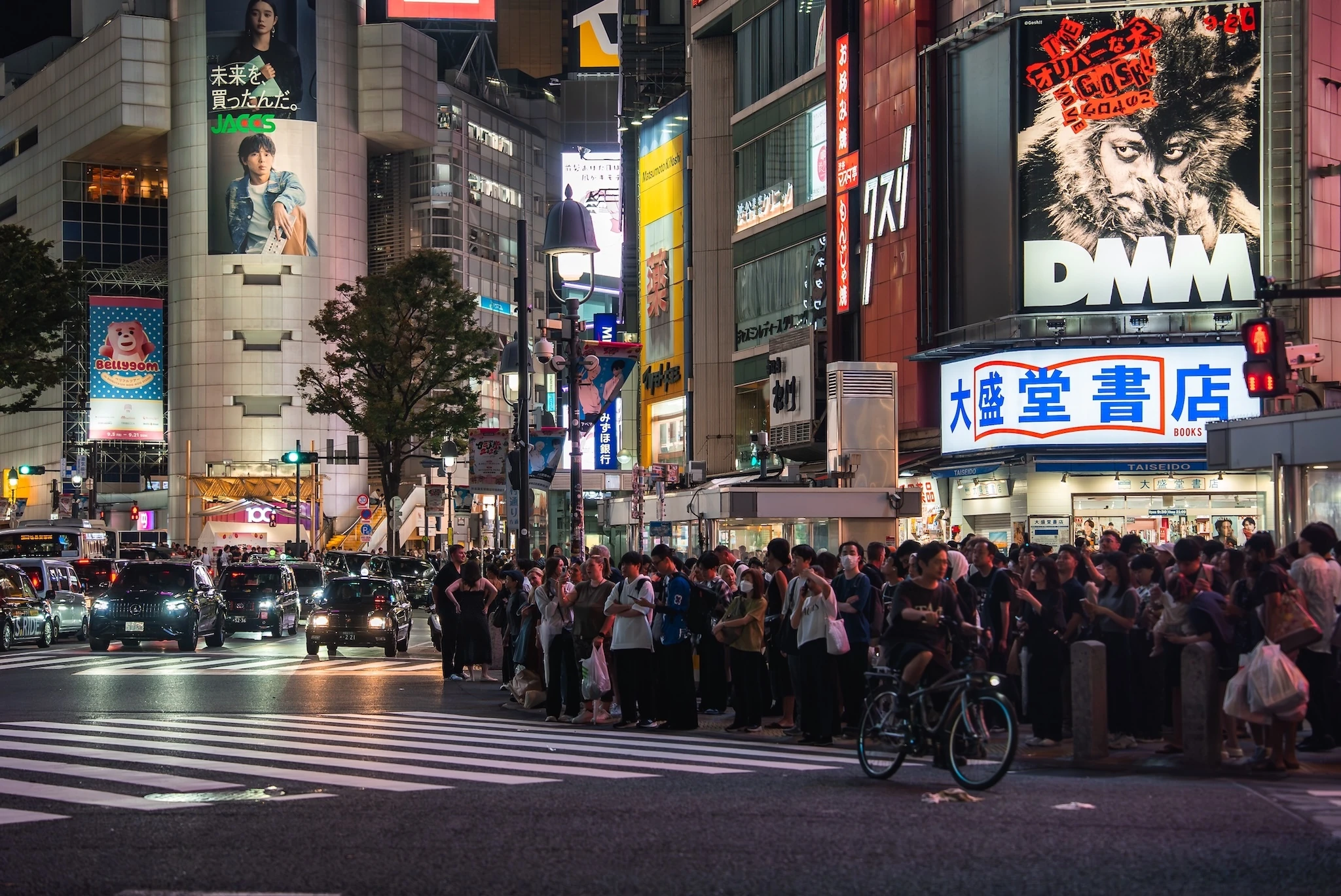 Crowds wait at a Shibuya, Tokyo crosswalk as taxis and cars queue