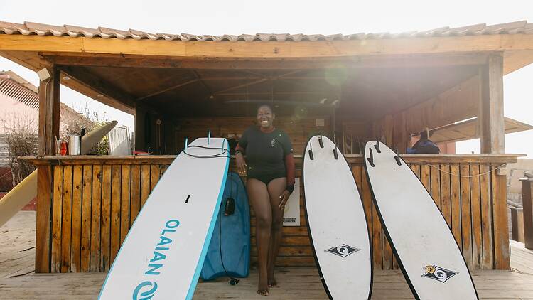 A woman stands with surfboards on a beach in Dakar, Senegal