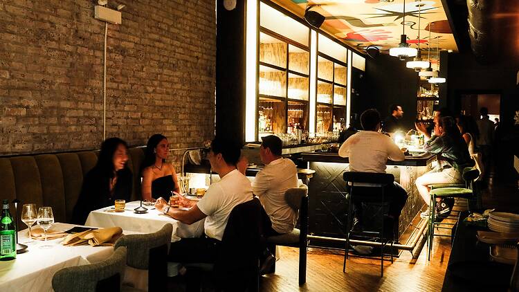 Diners sitting in a dining room and around a bar, under a painted mural.