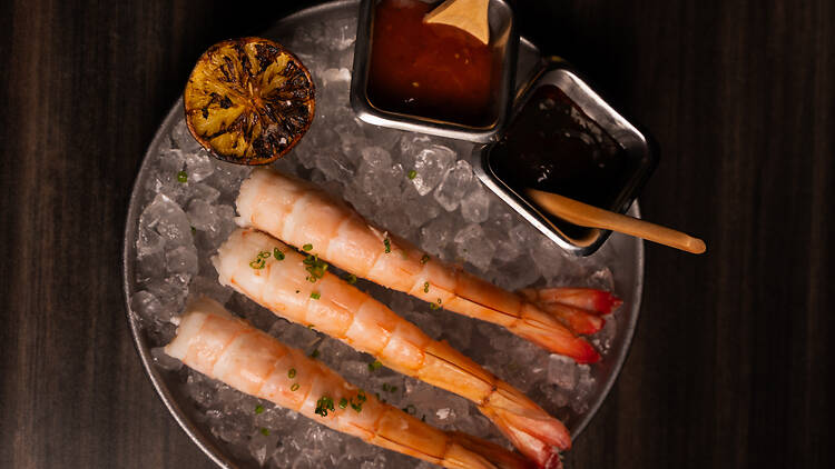 Three pieces of shrimp and cocktail sauces served over a bed of ice.