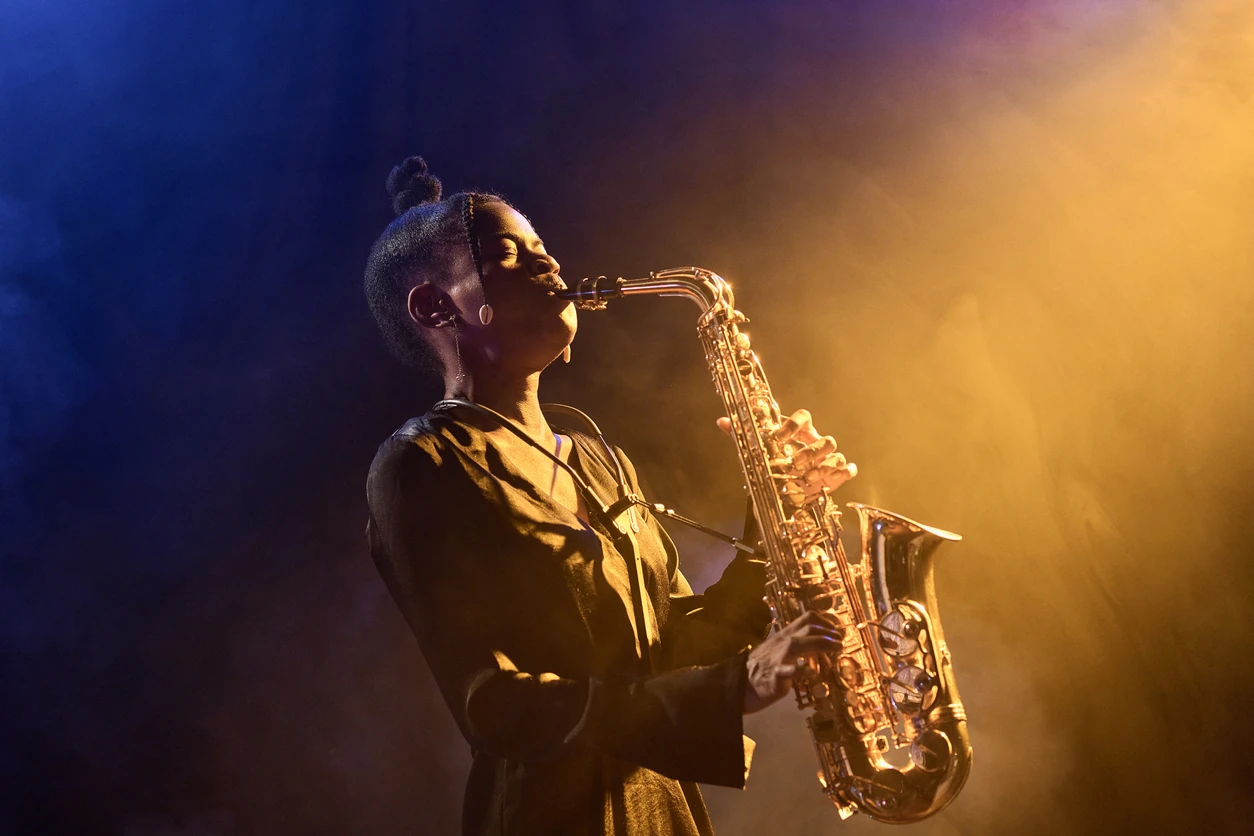 Portrait of passionate Black woman musician playing saxophone in jazz nightclub with golden hazy light copy space