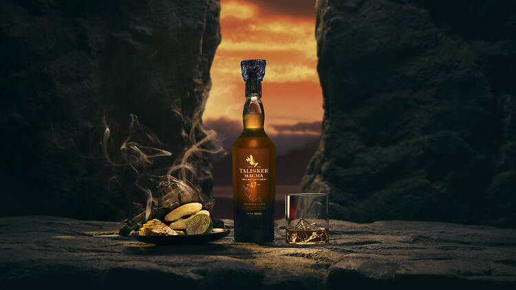 Talisker A whisky bottle, glass and plate of food in front of a sunset