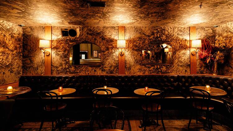 A dimly lit room with floral wallpaper and tables for two.