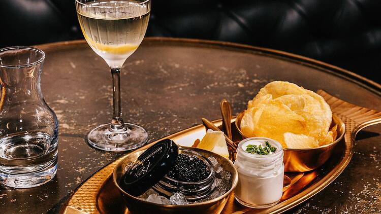 A martini next to a tray of caviar with chips.
