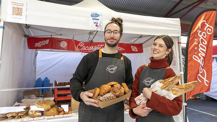 man holding box of croissants, woman holding baguettes