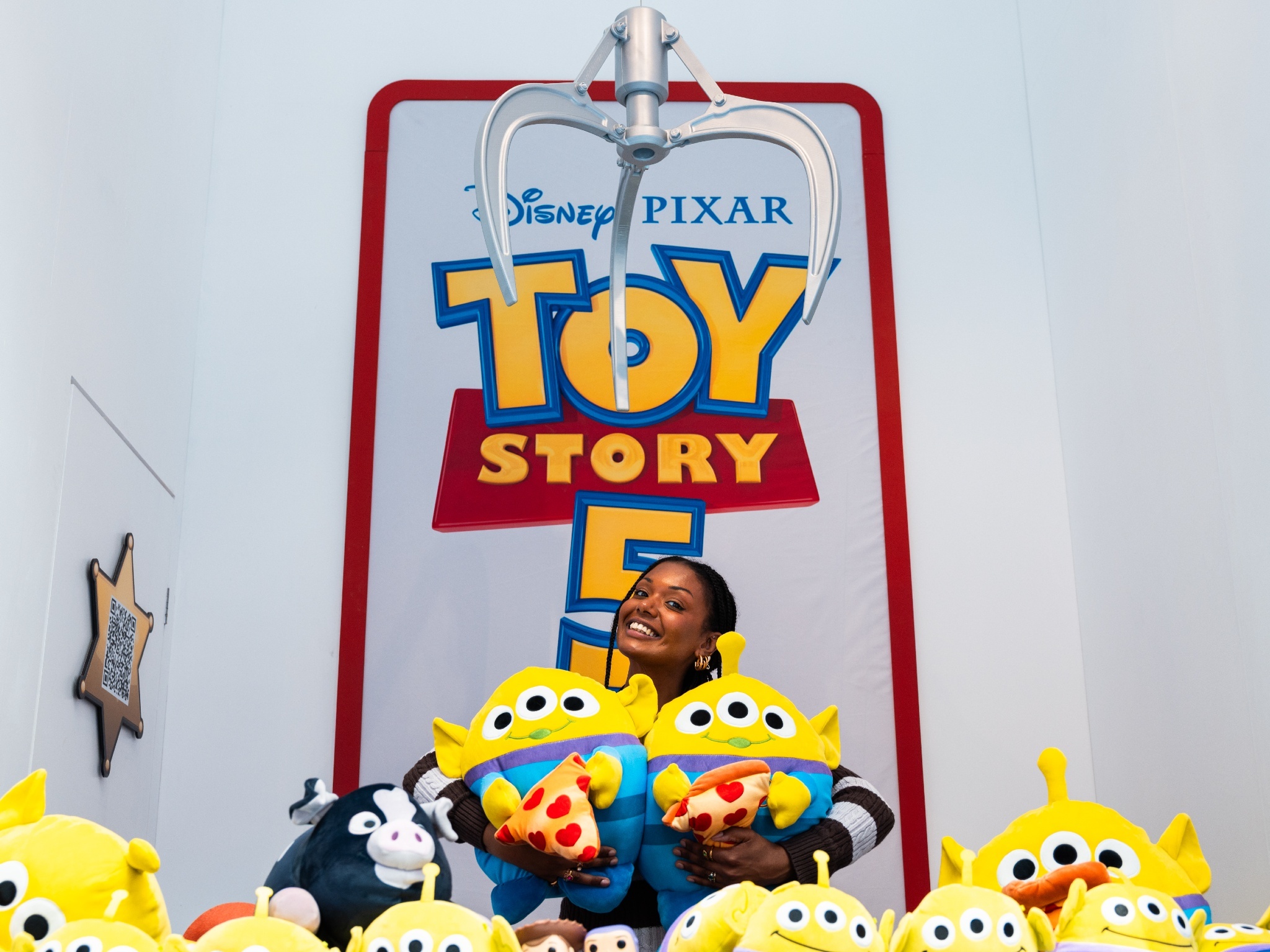 A woman poses with alien toys inside a claw machine at a Toy Story 5 pop-up at Westfield
