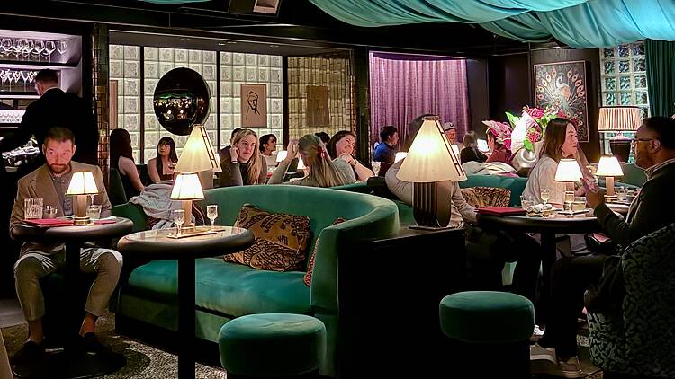 A cocktail lounge featuring emerald green booths, drapery hanging from the ceiling and lamp lighting. A cocktail lounge featuring emerald green booths, drapery hanging from the ceiling and lamp lighting.