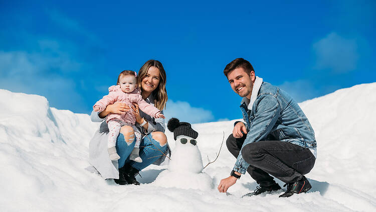 mother, father and baby with a snowman in the snow