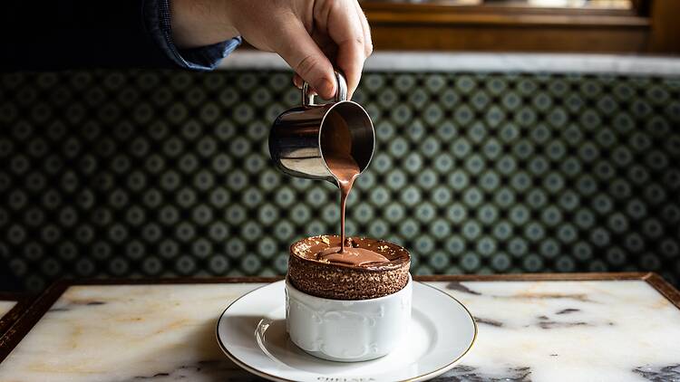 A person pouring chocolate sauce over the dessert