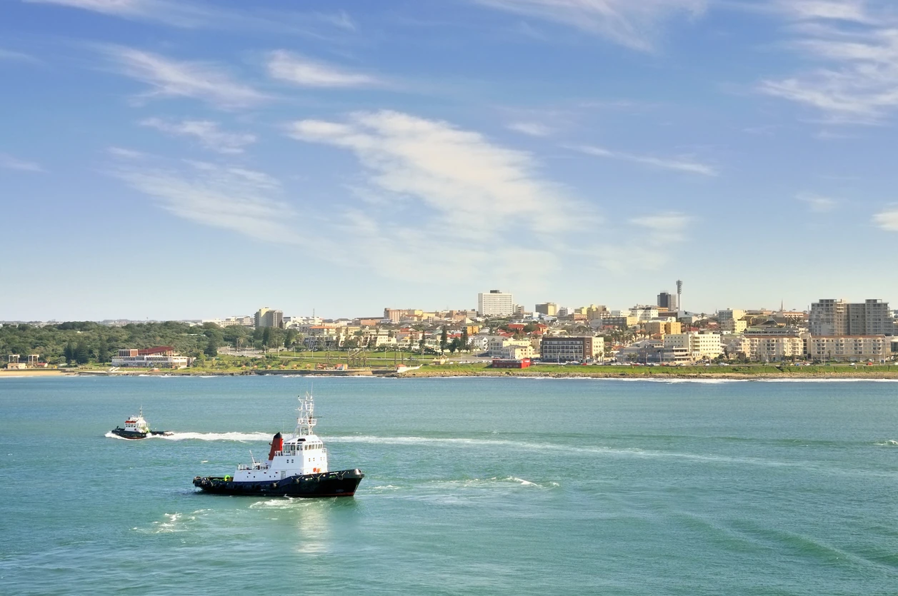 Tugboats scurry around the water front of the East London SA harbor in the Buffalo River with waterfront residences along the shoreline in the background