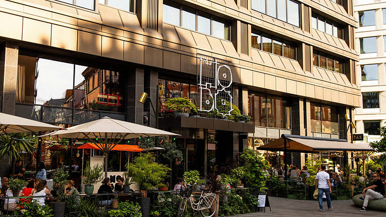 Hobo, Strawberry The exterior entrance of Hobo Hotel in Stockholm, featuring a lively outdoor patio restaurant surrounded by lush green plants and umbrellas.