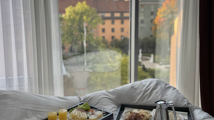 Amaranten An elegant hotel restaurant featuring set dining tables and distinctive, large circular windows overlooking a city view at dusk.