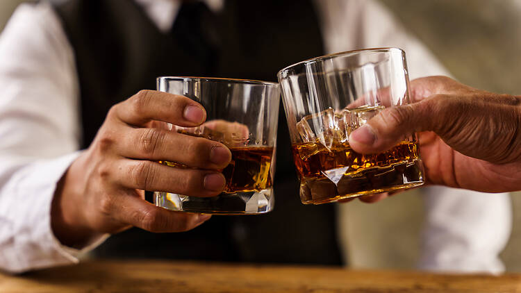 Two hands clink glasses of whiskey wiskey on the couch, cozy. Bar drinking menu.