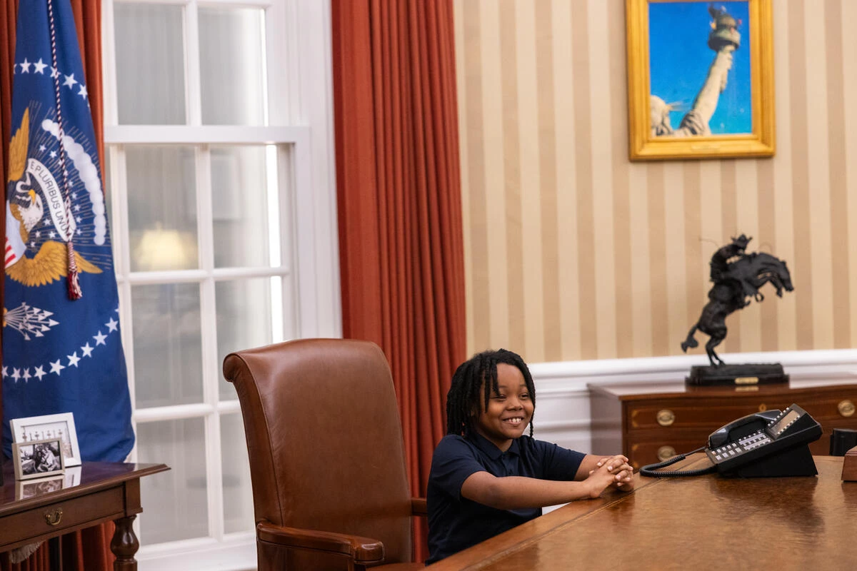 A child poses for a photo at the Resolute Desk in the Oval Office exhibit.