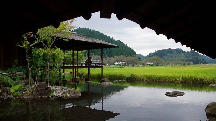Minamiaso, Japan The serene architecture of a rustic cafe in Minamiaso, Japan, with a covered walkway alongside a tranquil pond. A peaceful retreat in the Aso countryside, blending nature and design.