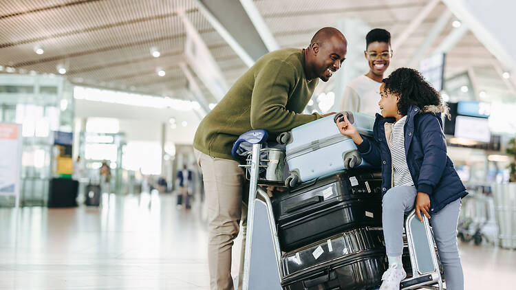 Family at airport with luggage Father and mother waiting with young daughter at airport. Tourist family at airport terminal with luggage holiday.