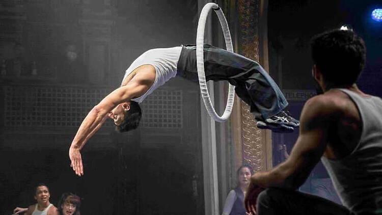 A wide shot of an acrobat backbending mid-air through a suspended ring A wide shot of an acrobat backbending mid-air through a suspended ring