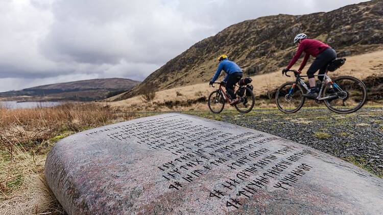 Two bikepackers pass The Giant Axe Head, near Loch Dee